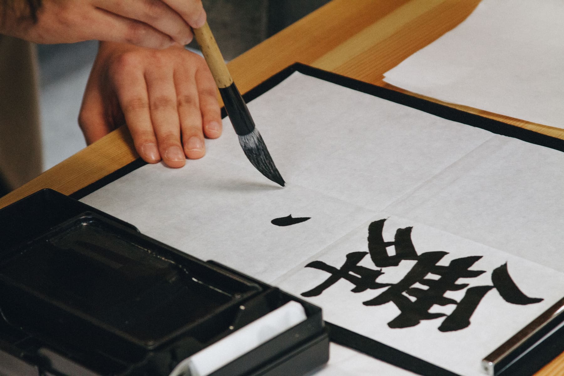 A hand writing a kanji with a brush on paper