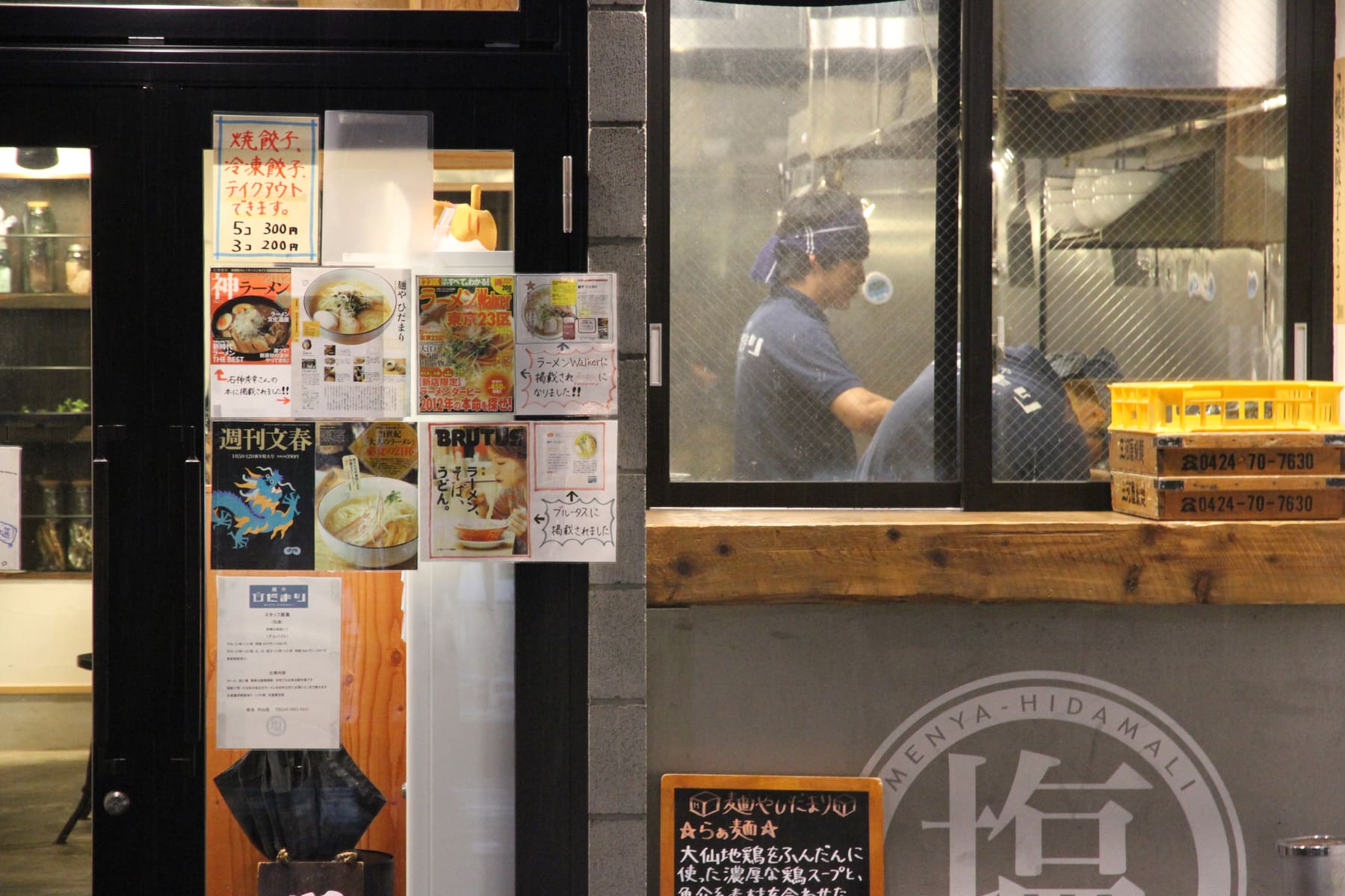 The entrance of a ramen shop in Tokyo with menu photos and cooks seen through the window