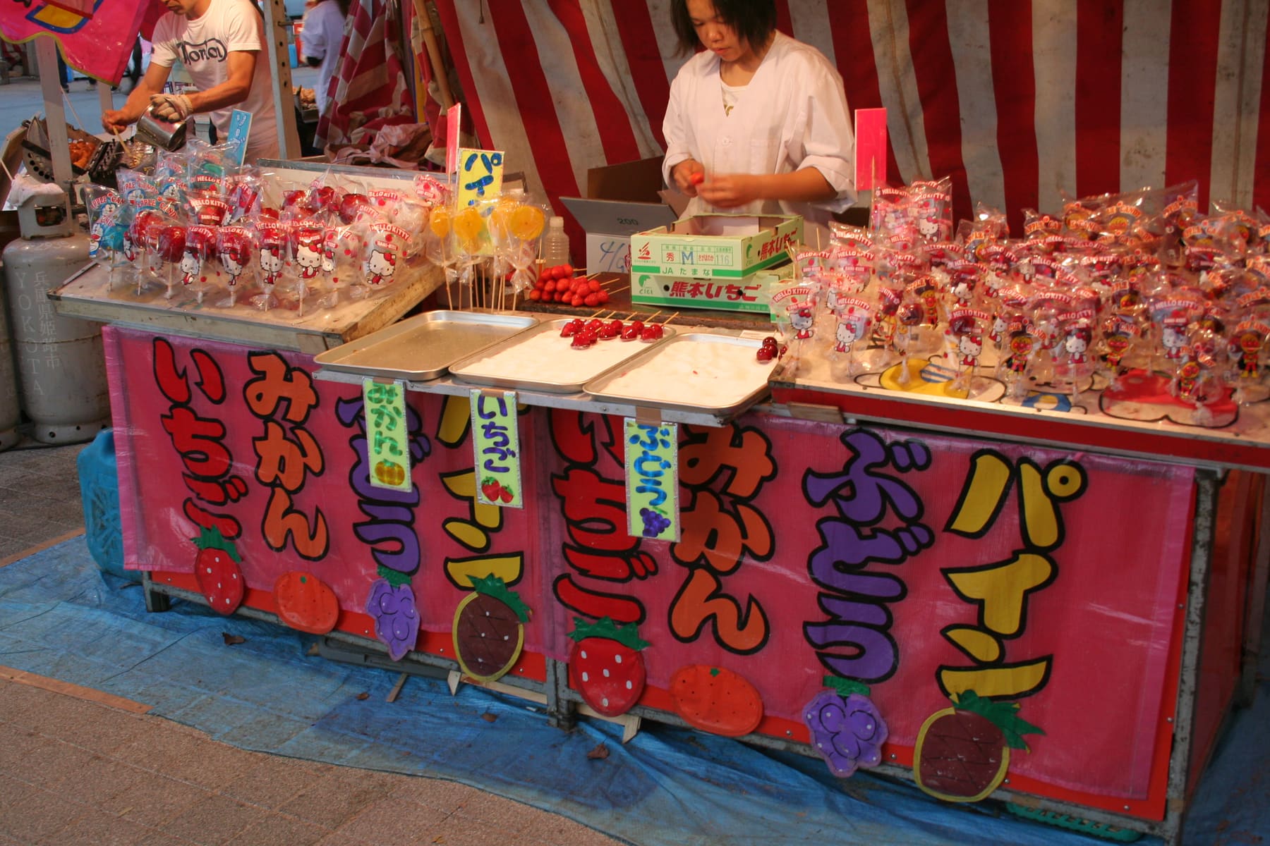 A festival food stall with fruit names in kana on colored boards