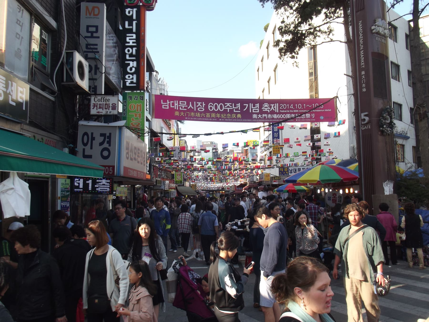 A crowded shopping street at Namdaemun Market in Seoul under a festival banner, with Korean shop signs
