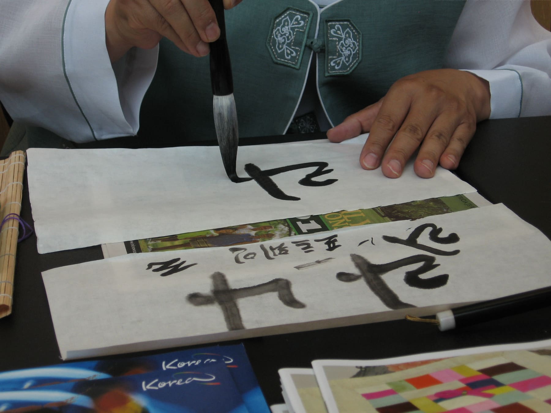 A calligrapher writing Hangul letters with a brush on paper