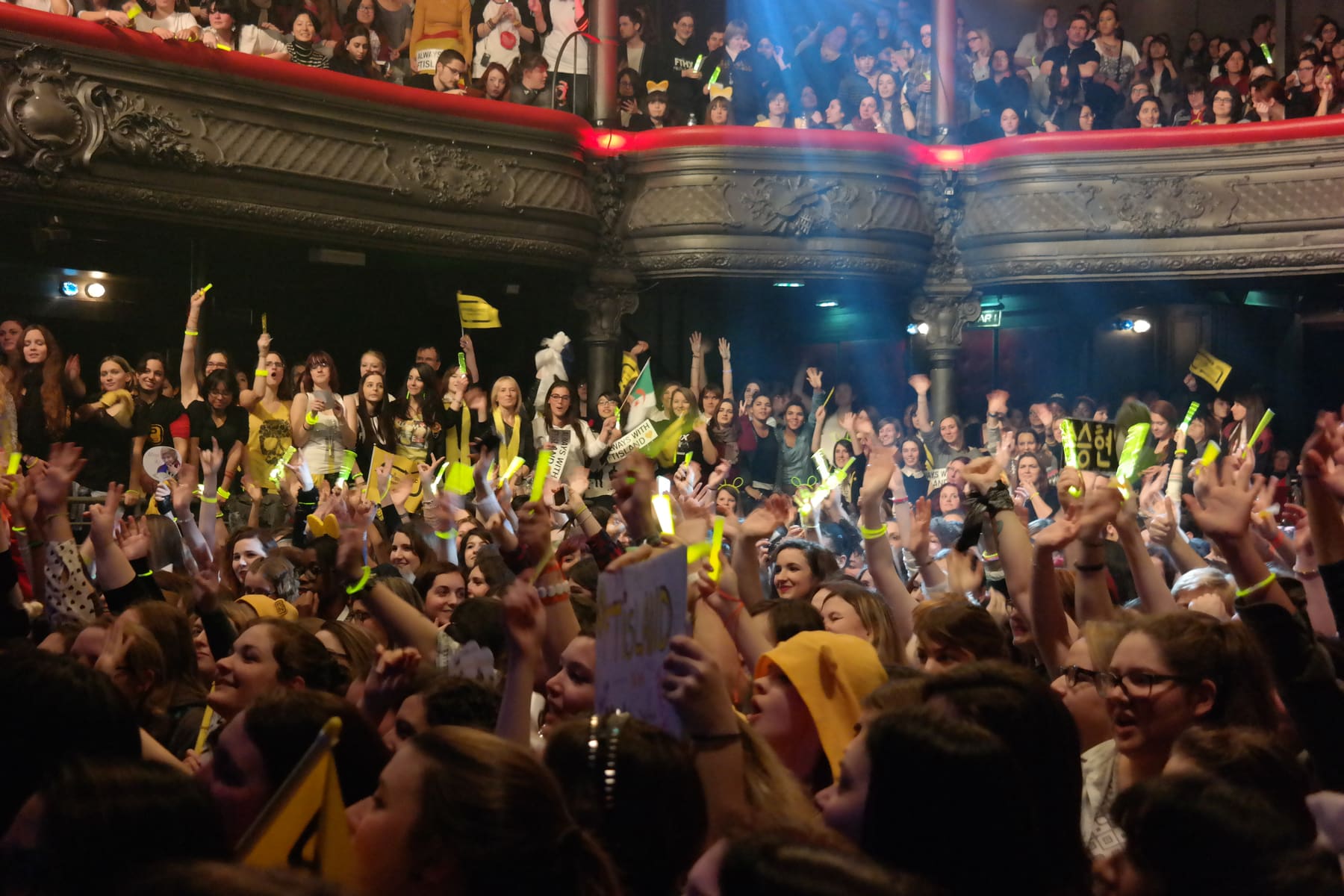 Fans with yellow light sticks raising their arms at a K-pop concert in Paris