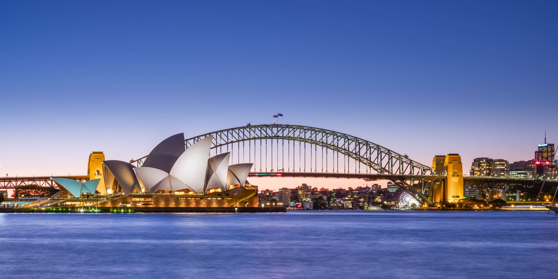 The Sydney Opera House and Harbour Bridge at dusk, lit against a purple sky