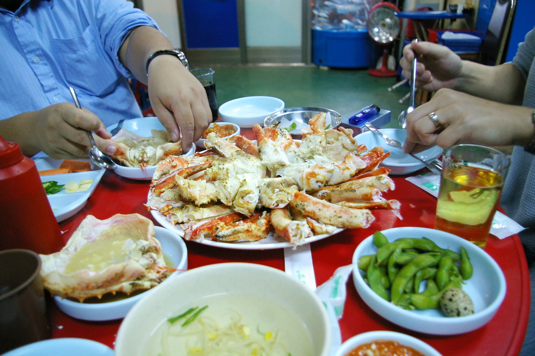 Hands reaching for a shared plate of steamed crab at a Korean restaurant table