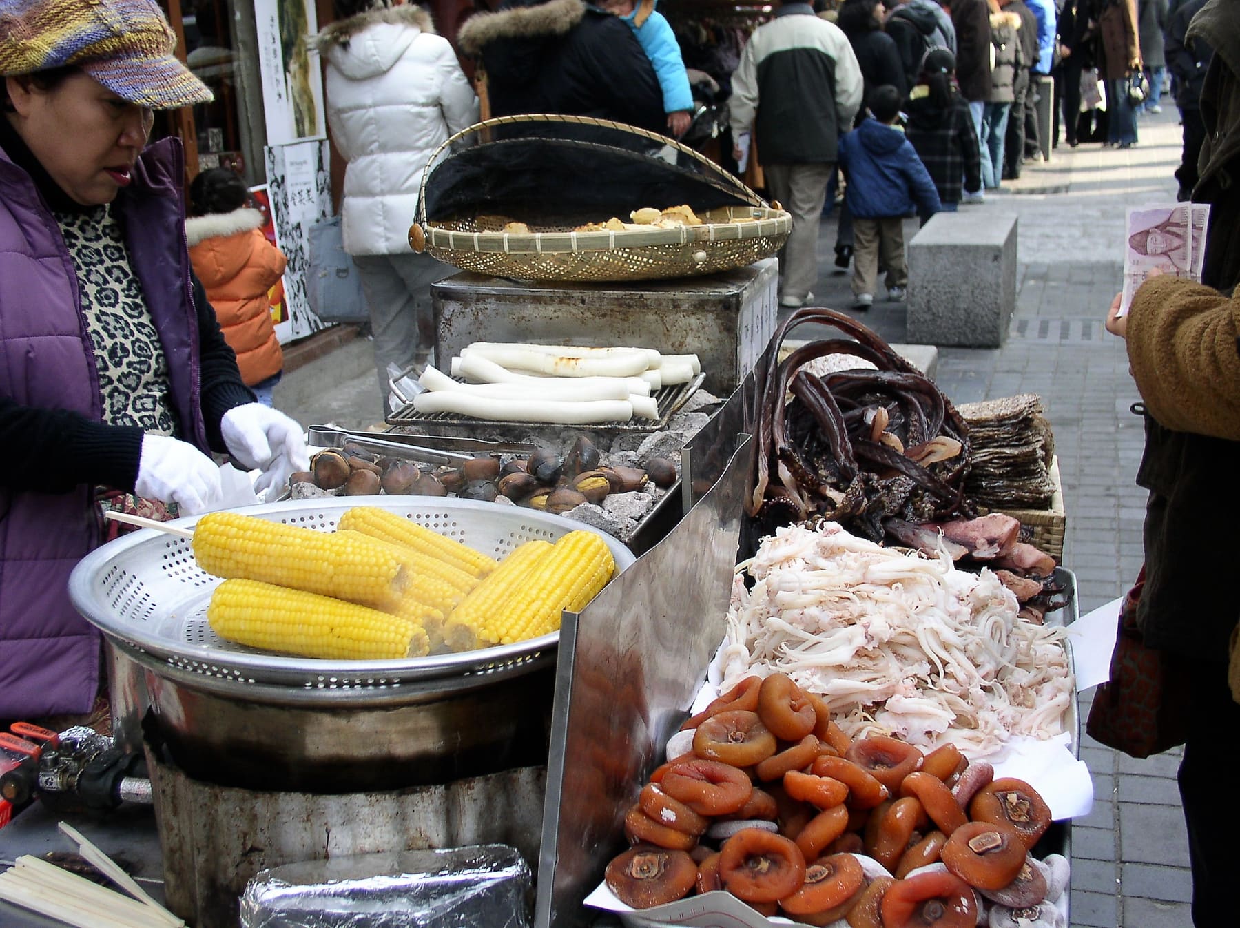 A street vendor selling corn and snacks from a stall on a busy Seoul street