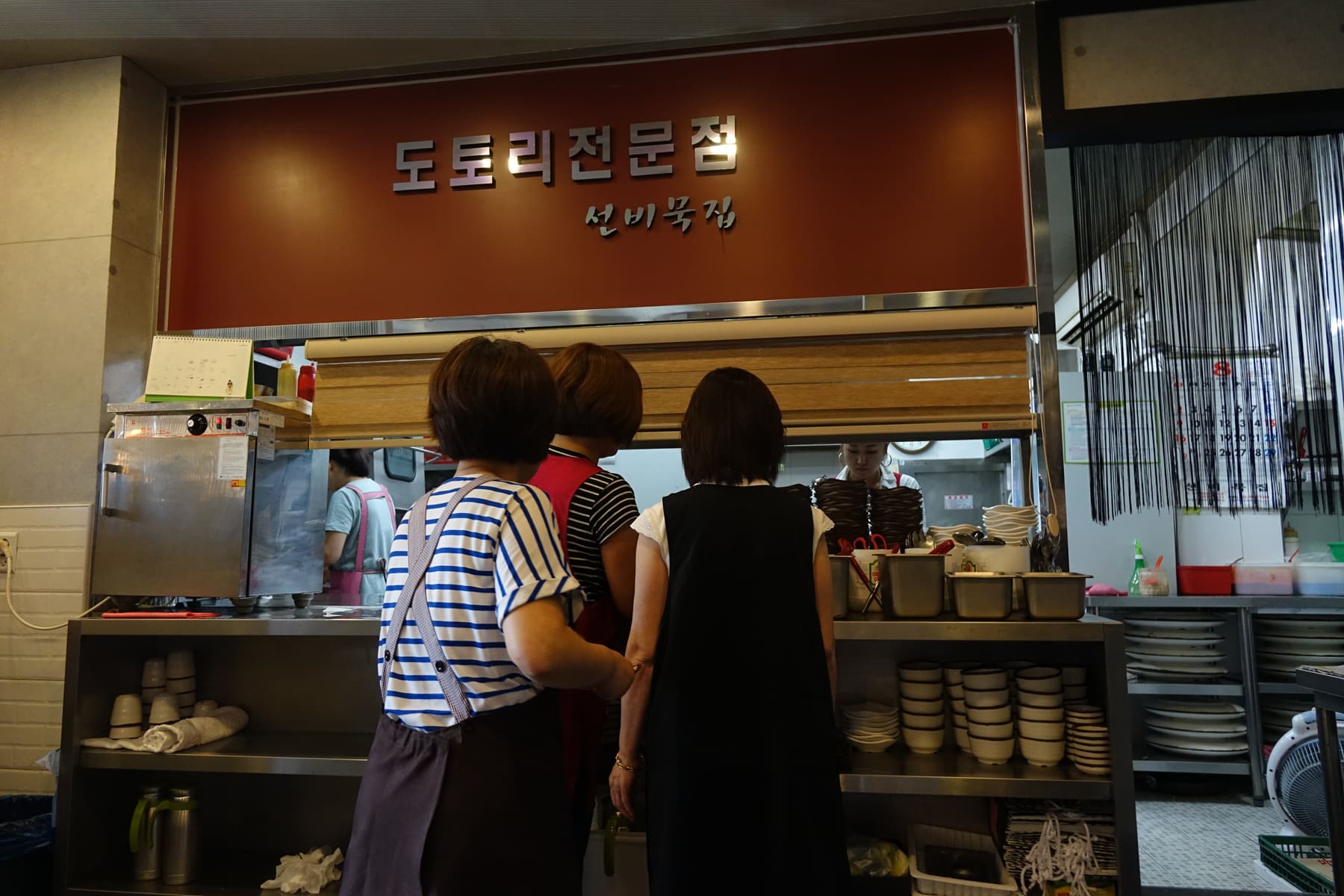 Customers seen from behind at the counter of a Korean restaurant under a Hangul sign